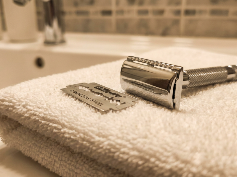 Stainless double edge razor blade resting on a folded towel beside a chrome safety razor