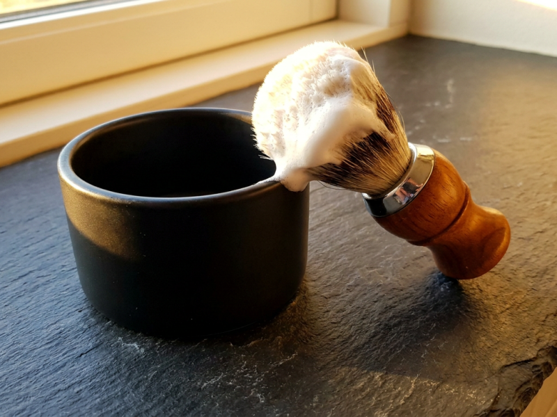 House of Mammoth soap review, a plain unmarked artisan shaving soap tub beside a badger brush loaded with thick white lather