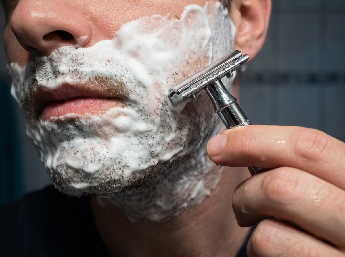 Close-up of a face covered in shaving lather mid-shave with a chrome safety razor
