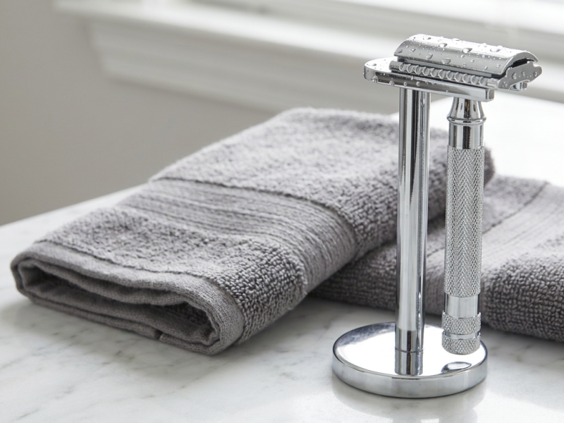 safety razor stand in polished chrome holding a double edge safety razor upright to dry on a marble counter