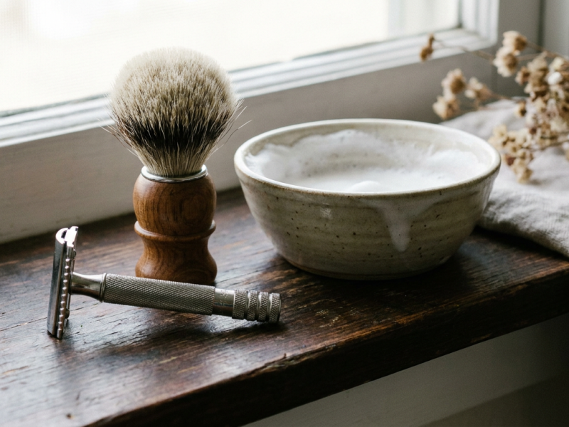 Beginner wet shaving kit with safety razor, brush and shaving soap on a wooden shelf